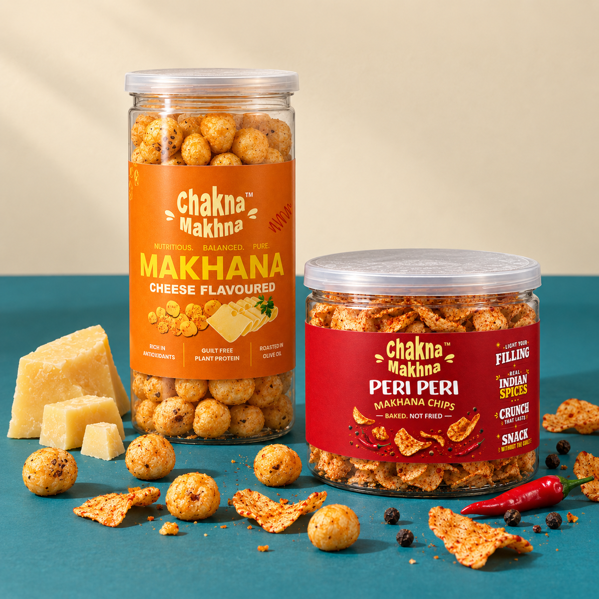 Two jars of Chakna Makhta snack mix displayed on a teal surface with cheese, chips, and chili peppers around them. The larger jar has an orange label and is labeled Makhana Cheese Flavoured, while the smaller jar has a red label and is labeled Peri Peri Makhana Chips.